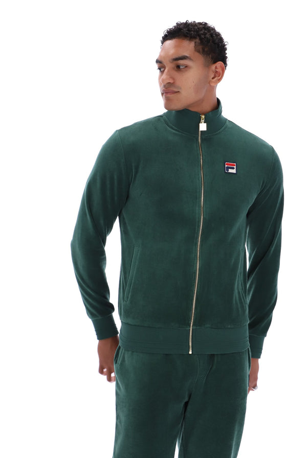A man wearing a dark green Fila zip-up track jacket and matching track pants, photographed against a plain white background.