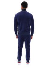 A man viewed from the back wearing a navy blue velour tracksuit with a mock neck jacket and matching pants, paired with white sneakers.