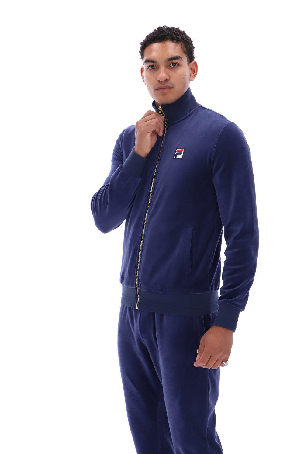 A man wearing a navy blue zip-up track jacket and matching sweatpants with a small Fila logo on the chest, photographed against a solid white background.