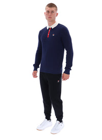 Man wearing a navy sweater with a red collar and black pants on a white background