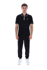 A man modeling a black short-sleeve polo shirt with white piping and a small red, white, and blue logo on the chest, paired with black sweatpants and white sneakers, against a plain white background.