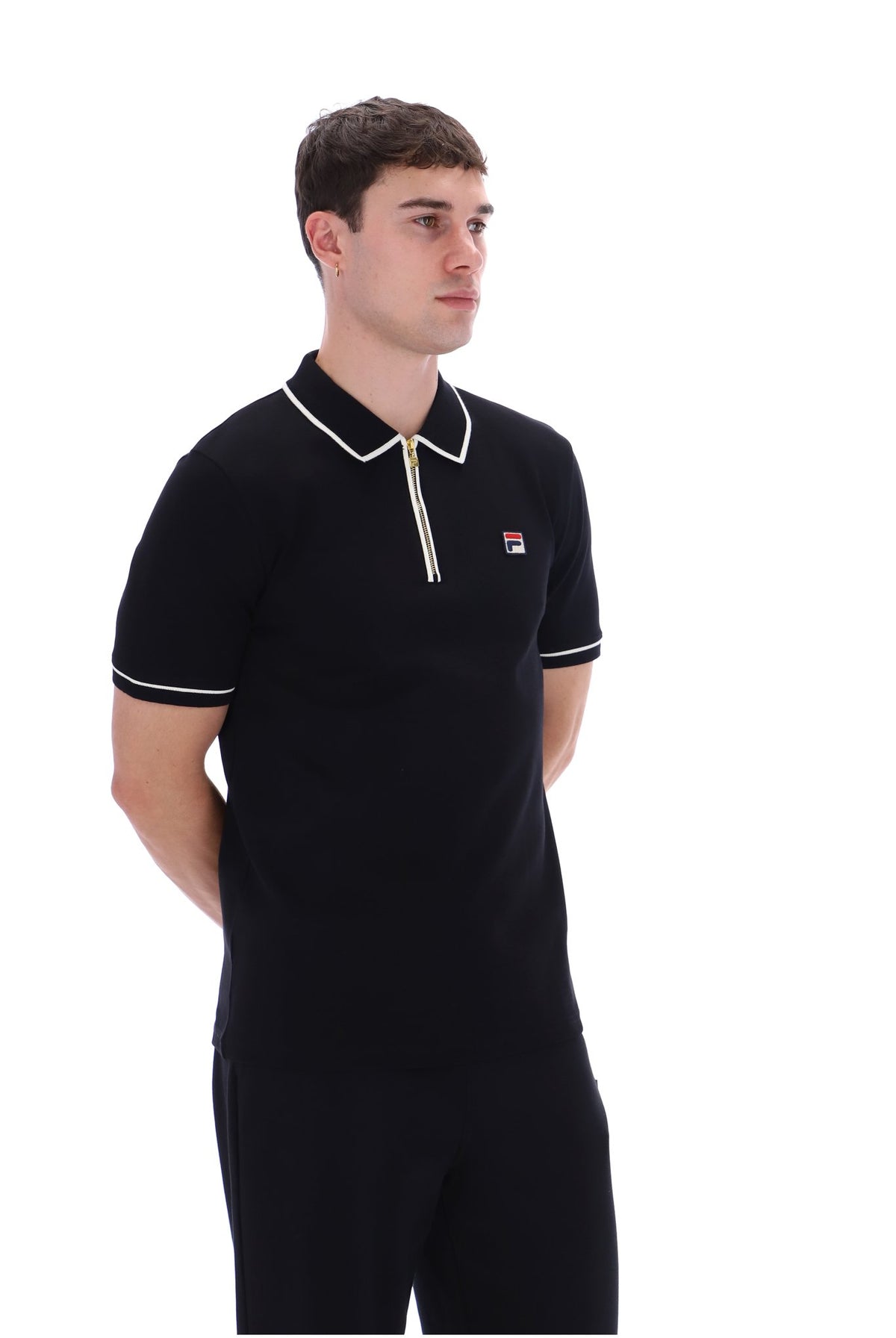 A man wearing a black short-sleeve polo shirt with white trim on the collar and sleeve cuffs, featuring a small Fila logo on the chest, set against a plain white background.