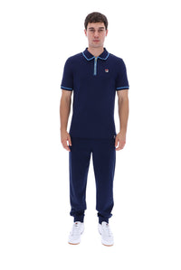 A man modeling a navy blue short-sleeve polo shirt with light blue trim and matching navy jogger pants, paired with white sneakers, against a plain white background.