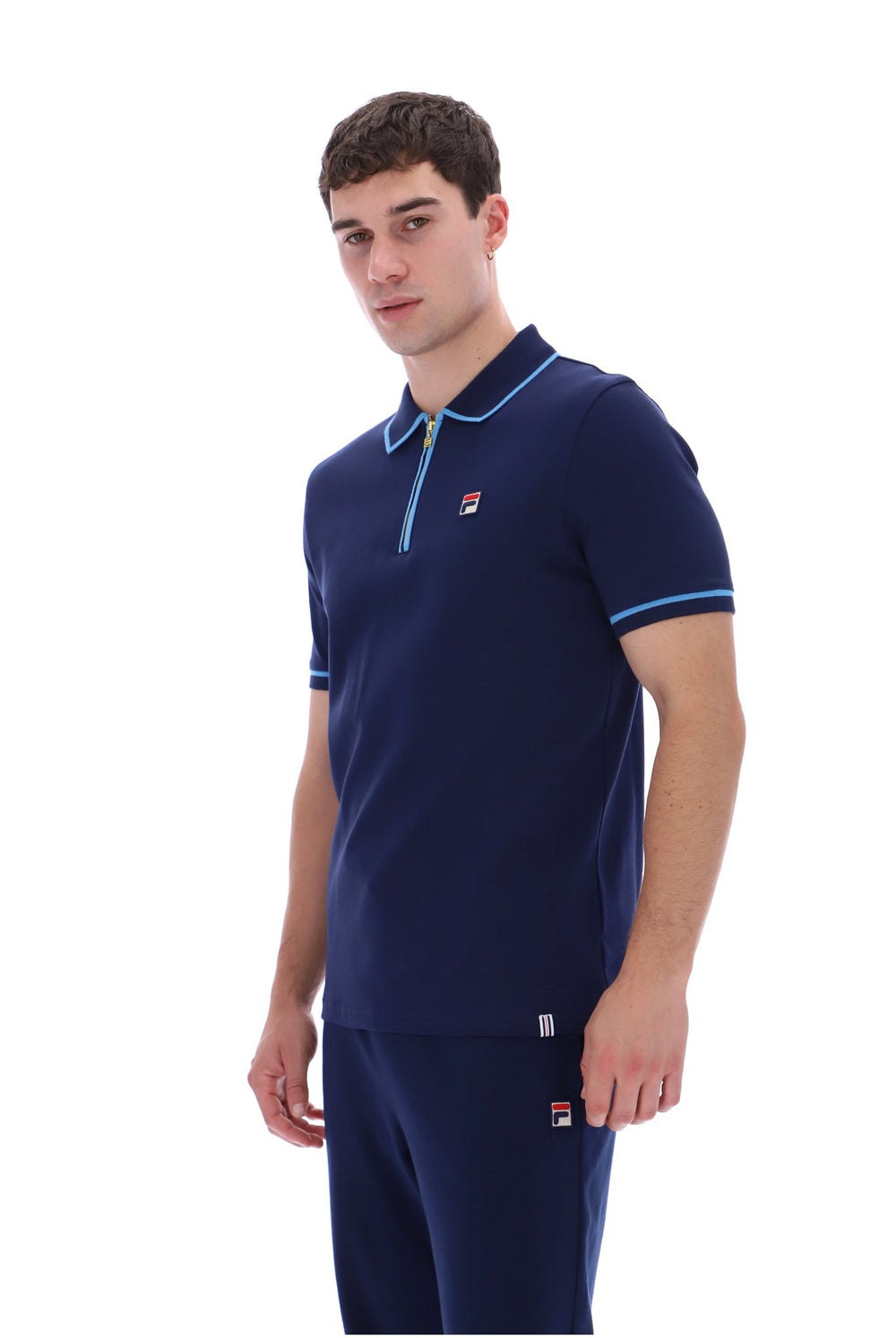 A man modeling a navy blue short-sleeve polo shirt with light blue trim and a matching navy pair of pants against a plain white background.