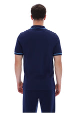 A man viewed from the back wearing a navy blue short-sleeve polo shirt with light blue trim on the collar and sleeve cuffs, paired with matching navy pants, against a plain white background.