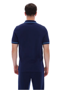 A man viewed from the back wearing a navy blue short-sleeve polo shirt with light blue trim on the collar and sleeve cuffs, paired with matching navy pants, against a plain white background.