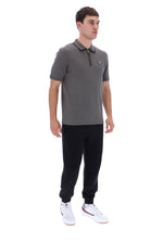 A man modeling a gray short-sleeve polo shirt with a black zipper collar, paired with black joggers and white sneakers, shot against a solid white background.