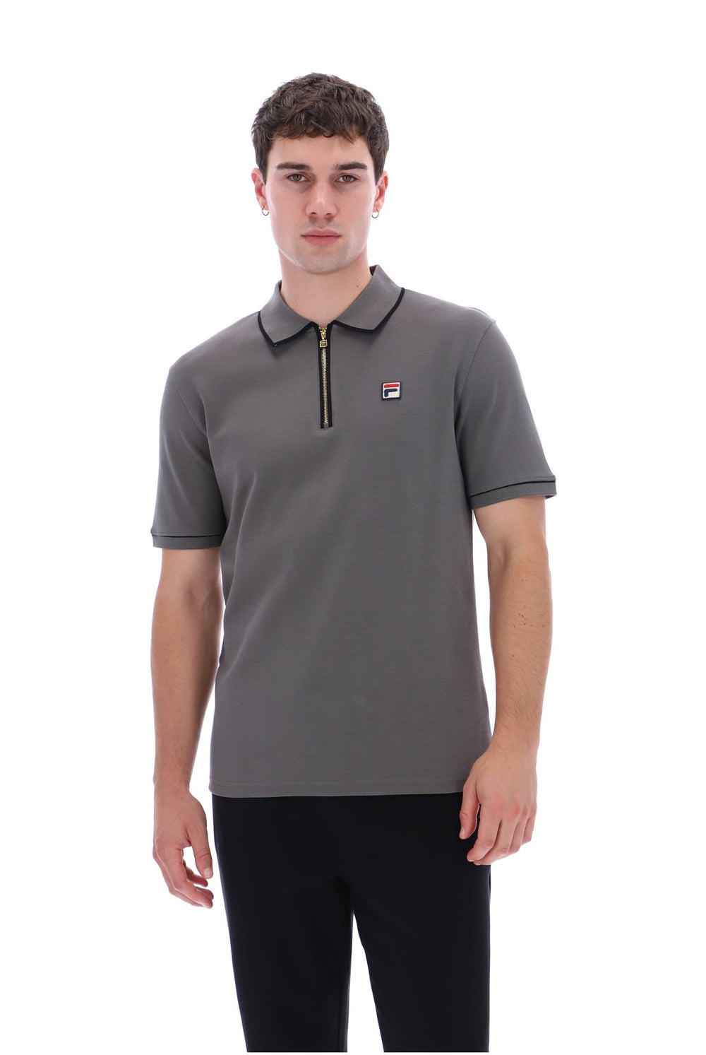 A man wearing a gray short-sleeve polo shirt with a half-zip collar and a small Fila logo on the chest, paired with black pants, against a plain white background.