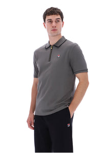 A man wearing a gray short-sleeve polo shirt with a black collar and zipper, featuring a small red, white, and blue Fila logo on the chest, paired with black pants against a white background.