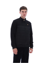 A man wearing a black zip-up fleece jacket with horizontal quilted puffer panels across the chest and a small gold embroidered logo on the left chest, photographed against a solid white background.