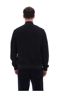 A man viewed from behind wearing a black long-sleeve knit sweater and dark trousers against a plain white background.