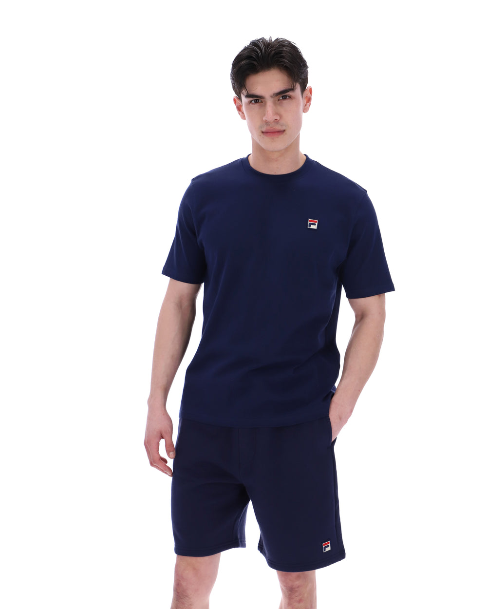 Man wearing a navy blue t-shirt and shorts set with a small FILA logo on a white background