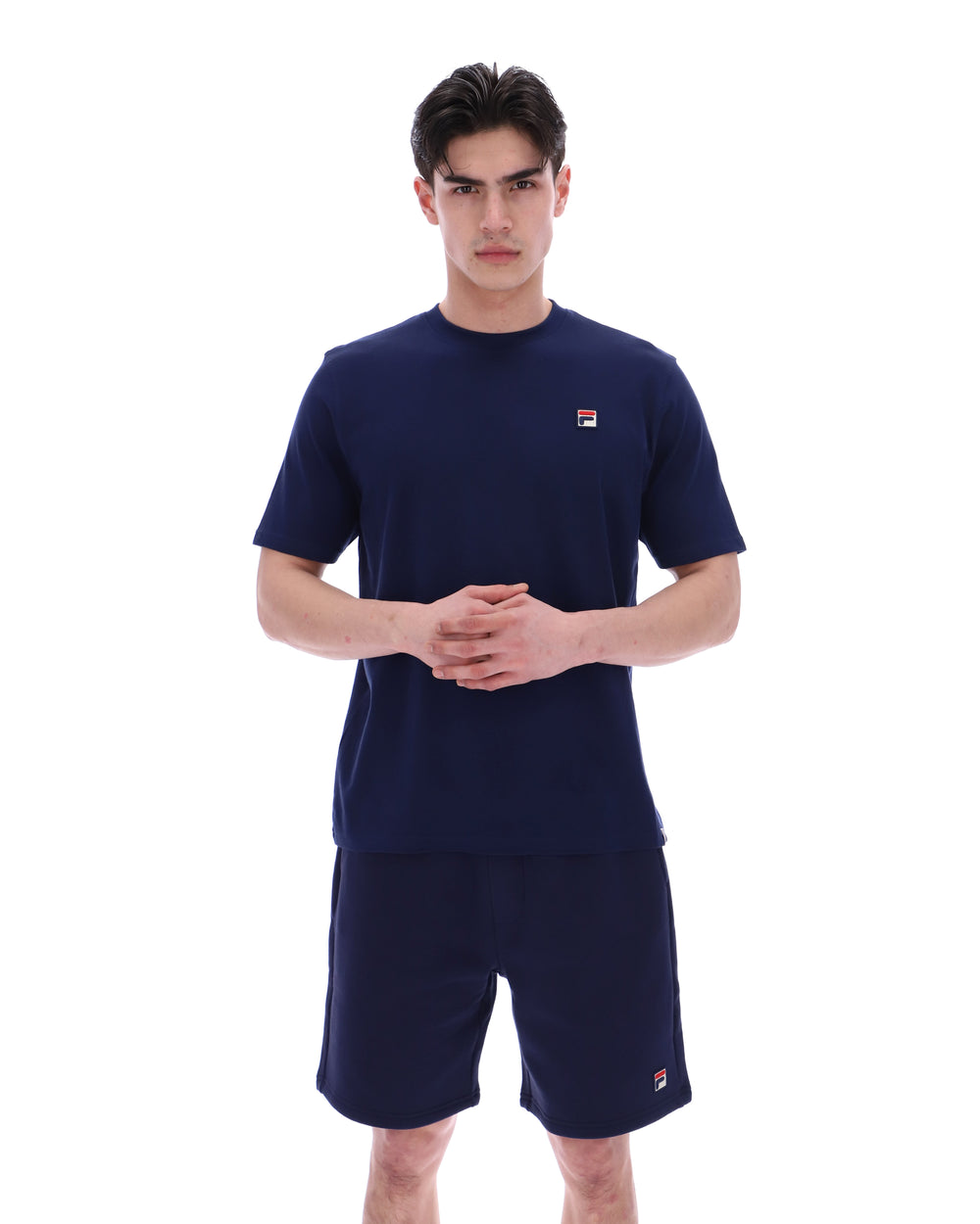 Man wearing a navy blue t-shirt and shorts set with a small FILA logo on a white background