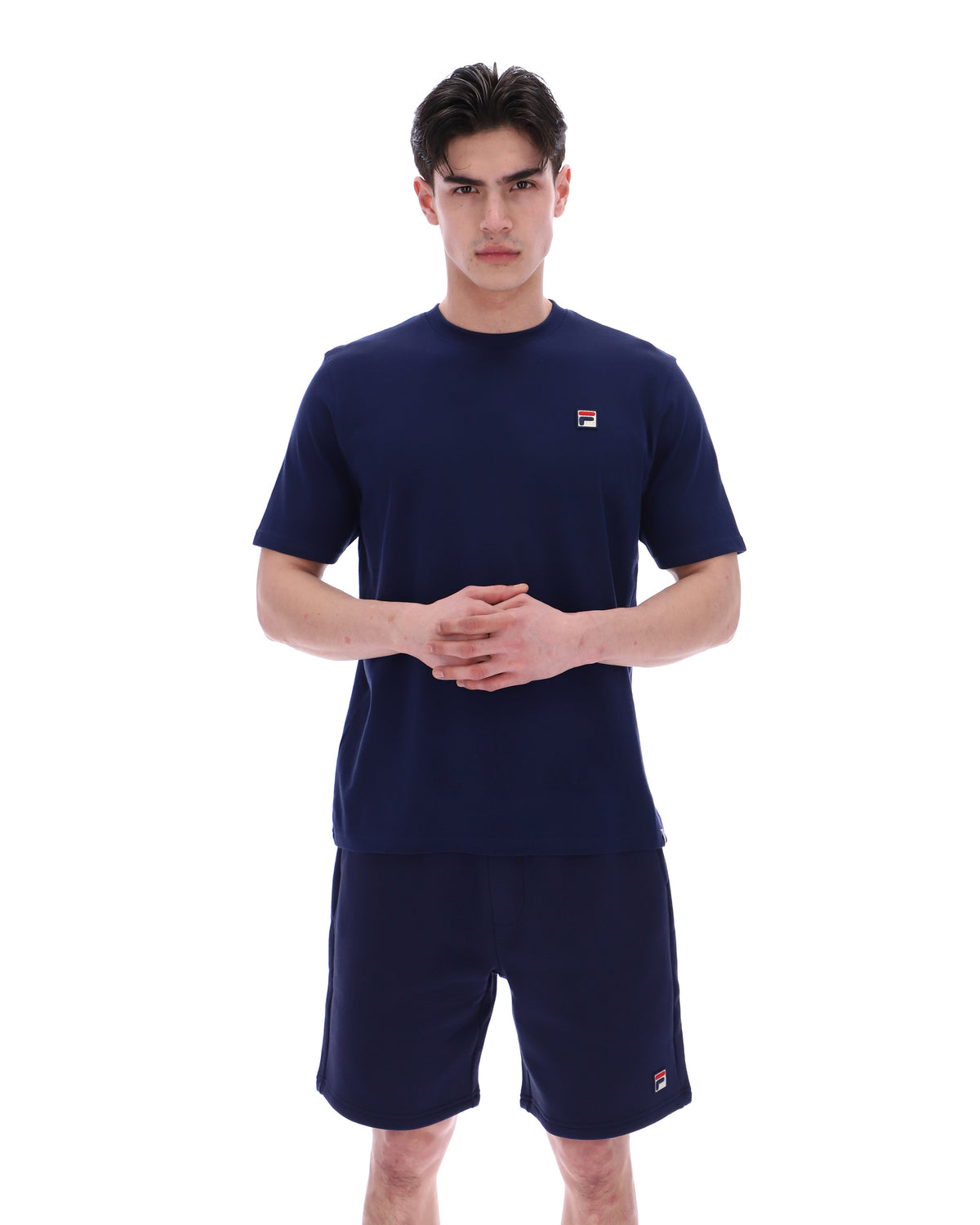 Man wearing a navy blue t-shirt and shorts set with a small FILA logo on a white background