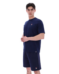 Man wearing a navy blue t-shirt and shorts set with a small FILA logo on a white background