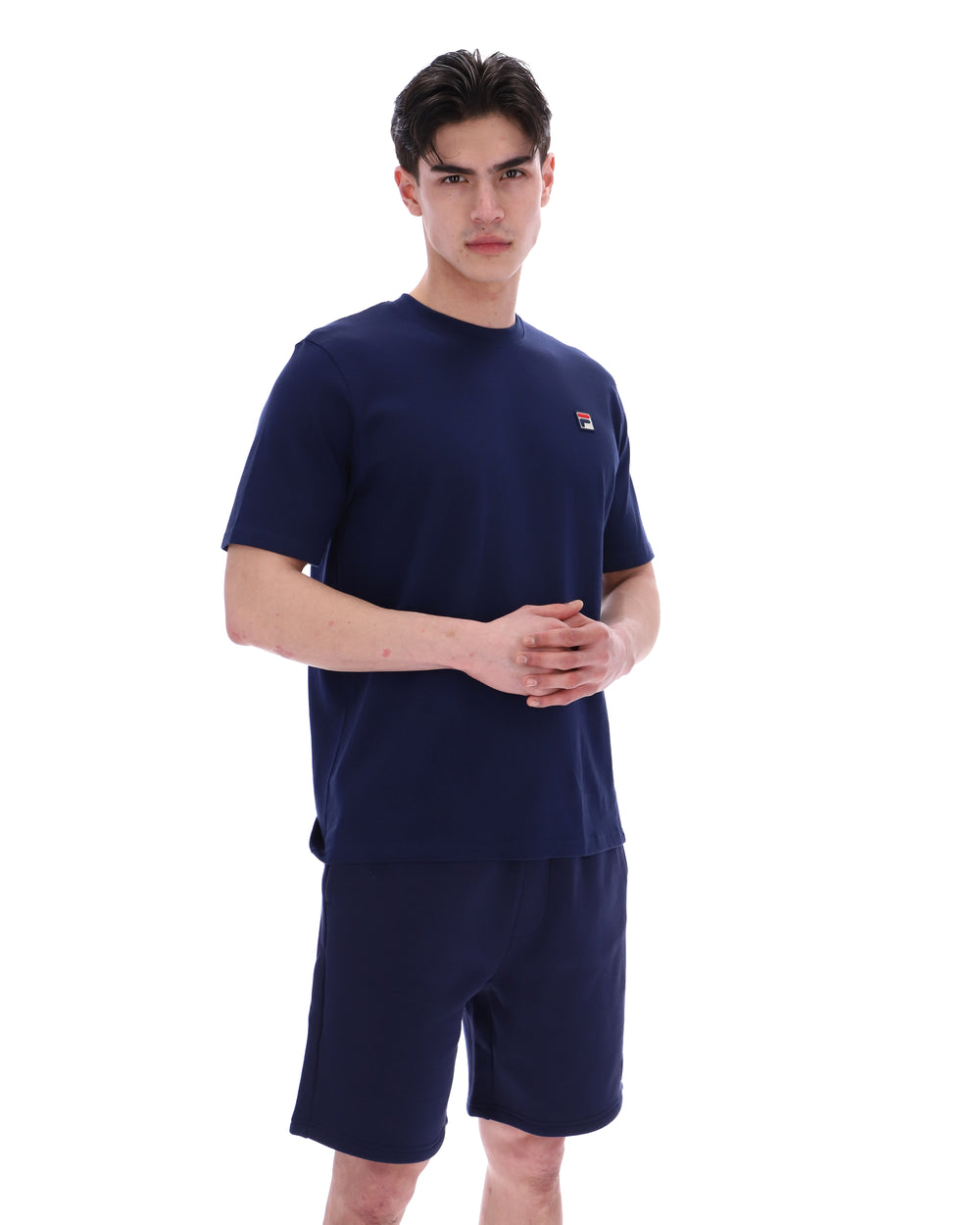 Man wearing a navy blue t-shirt and shorts set with a small FILA logo on a white background