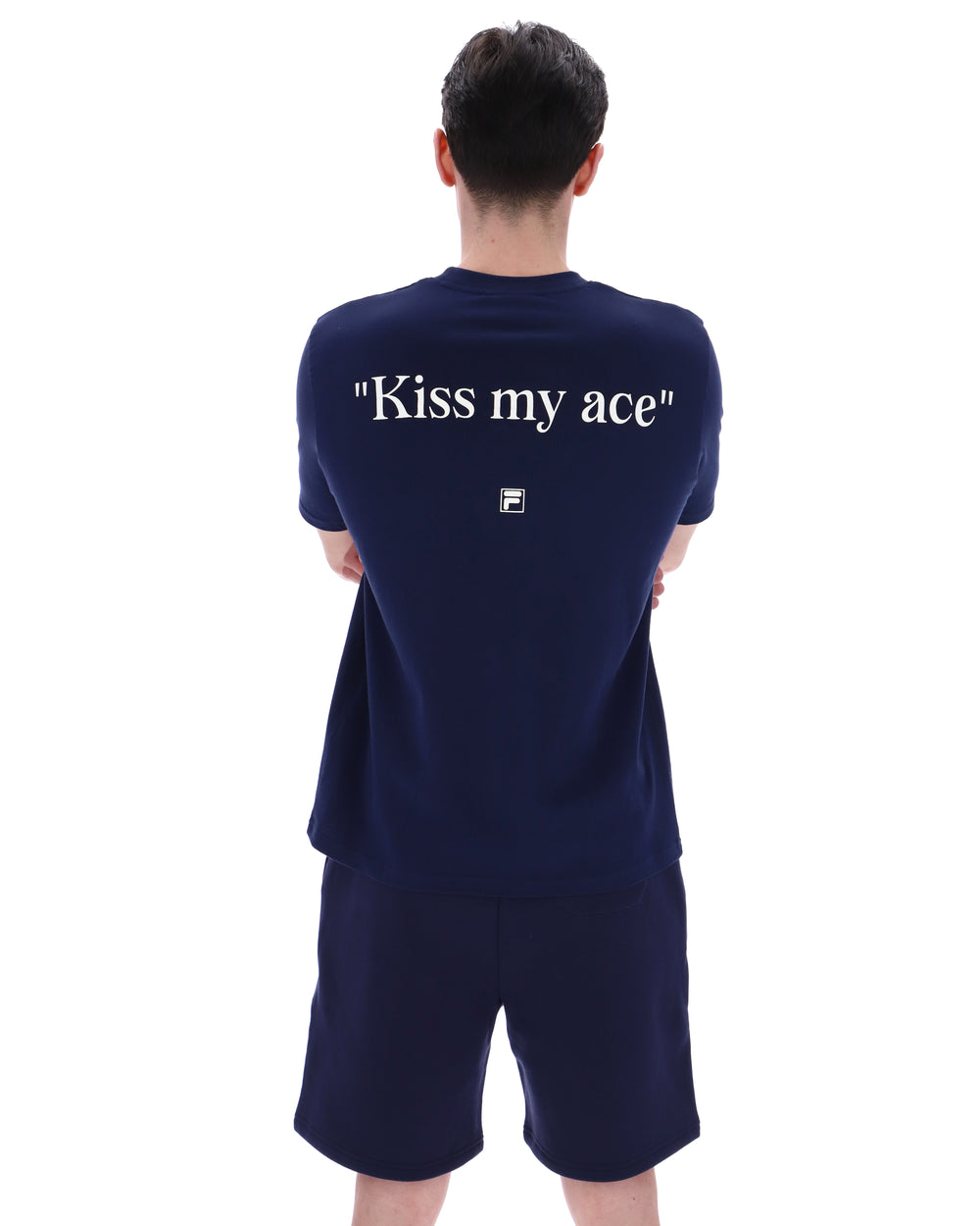 Person wearing a navy blue t-shirt with 'Kiss my ace' text on the back, standing against a white background
