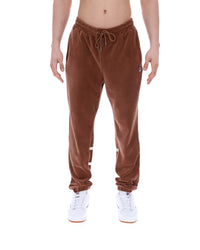 Brown velour jogger pants worn by a person on a white background