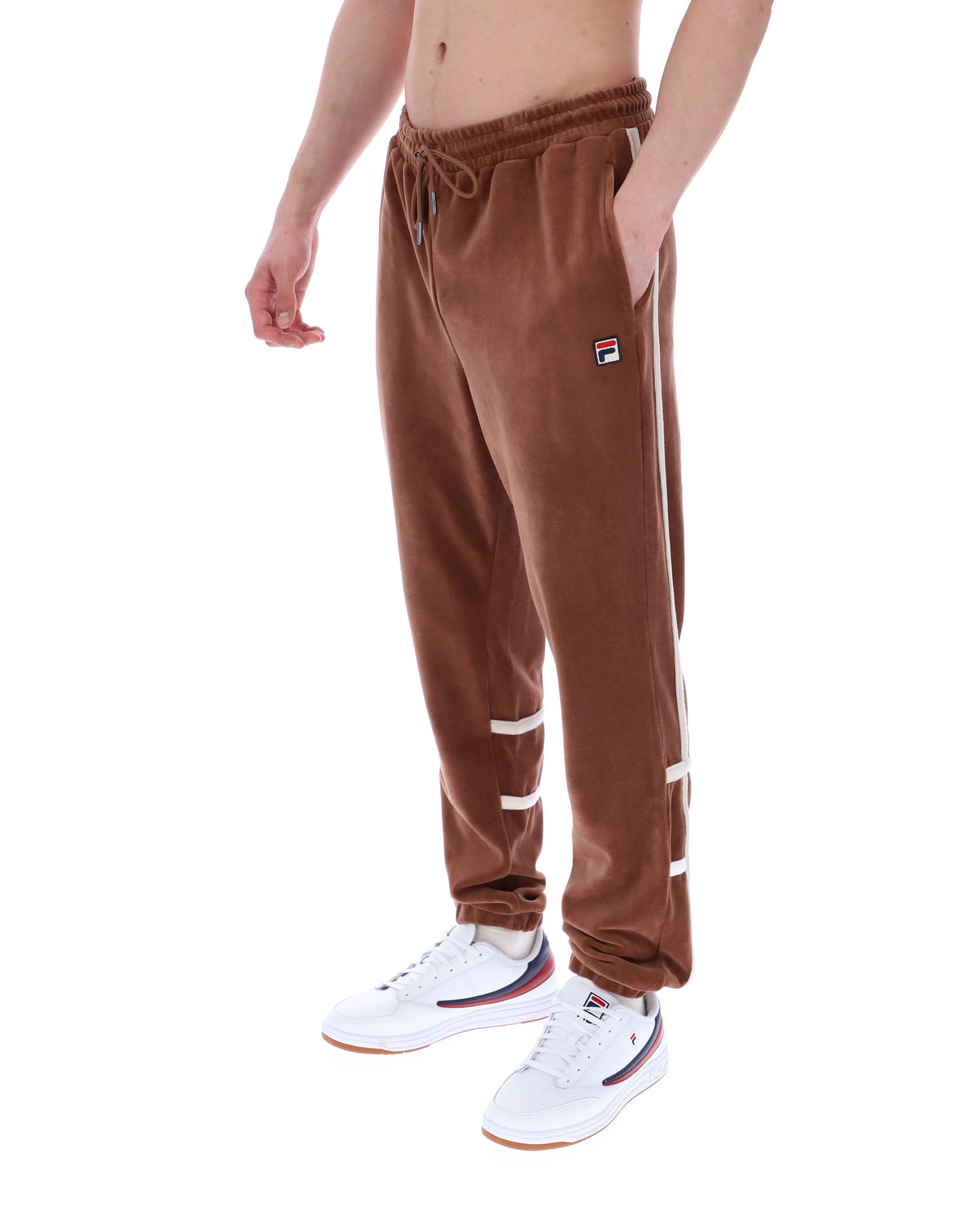 Brown sweatpants with white stripes and a FILA logo worn by a person on a white background