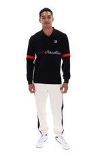 A man modeling a black long-sleeve polo shirt with red and white accents, paired with off-white track pants and white sneakers, against a plain white background.