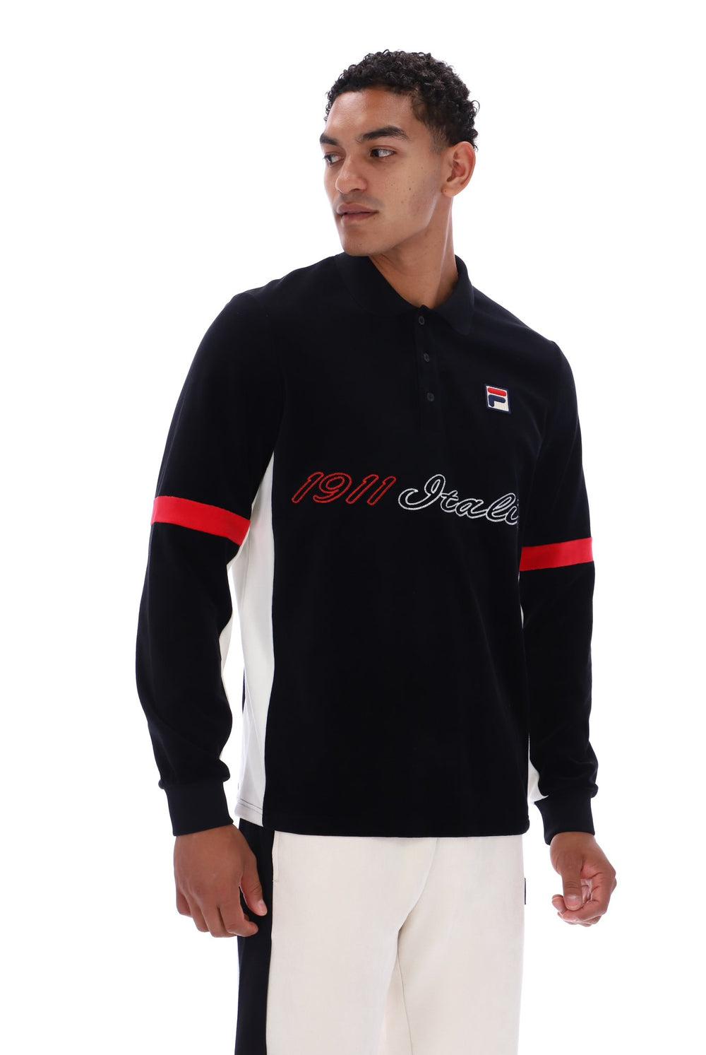A man modeling a black long-sleeve polo shirt with white side panels, red sleeve stripes, and '1911 Italia' text across the chest, paired with white pants against a white studio background.