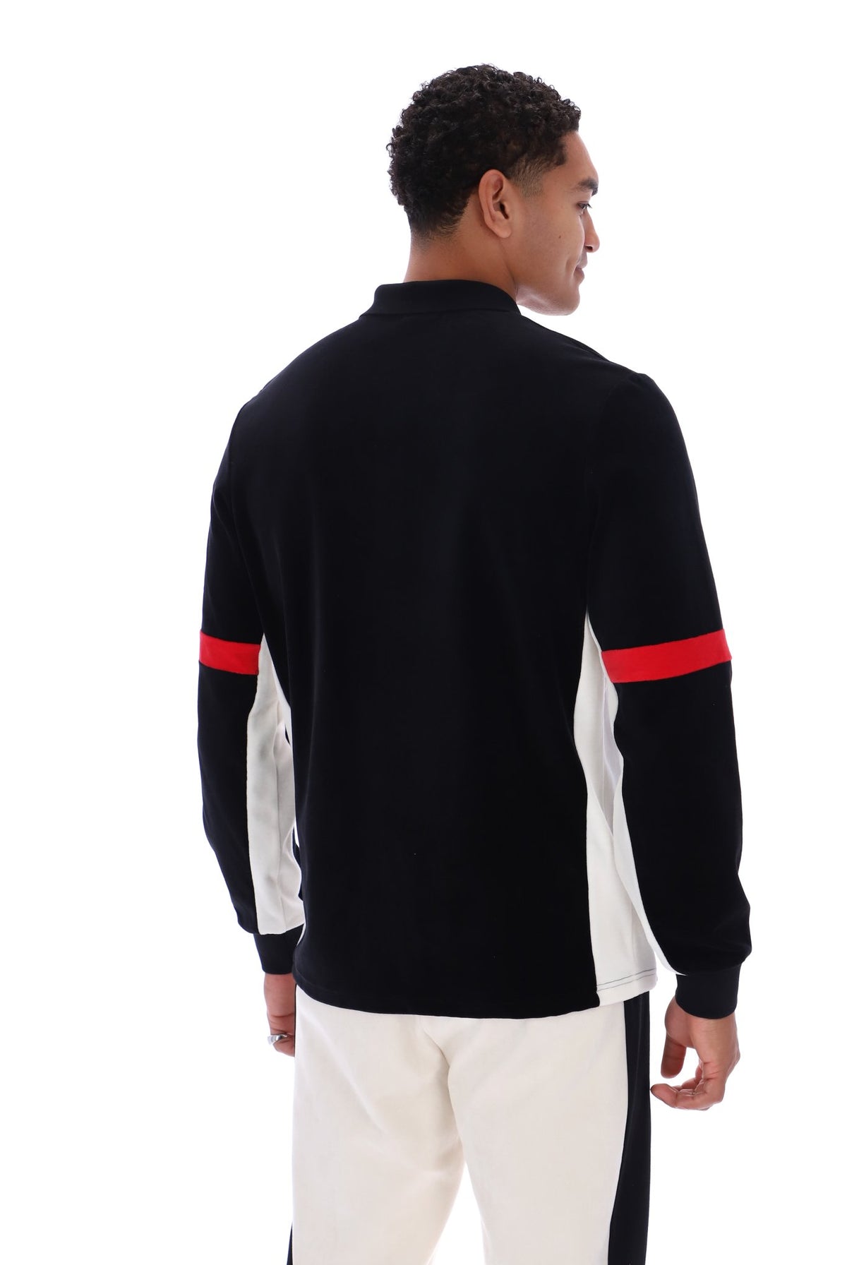 A man shown from the back wearing a black long-sleeve knit top with white side panels and red stripes on the upper arms, paired with off-white pants, against a plain white background.