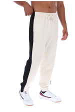 A person wearing cream jogger sweatpants with a bold black side stripe and white sneakers, shown from the waist down on a plain white background.