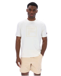 Man wearing a white t-shirt with a cream FILA logo printed on the chest and a classic FILA logo on the sleeve.