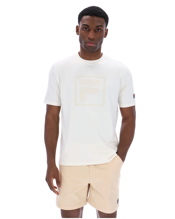 Man wearing a white t-shirt with a cream FILA logo printed on the chest and a classic FILA logo on the sleeve.