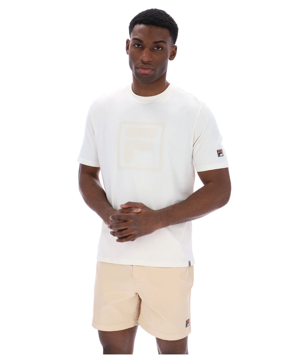 Man wearing a white t-shirt with a cream FILA logo printed on the chest and a classic FILA logo on the sleeve.