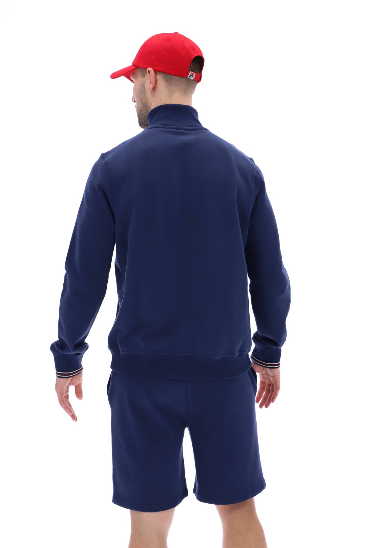 Man wearing a navy quarter zip jumper, paired with grey FILA jogger shorts, against a white background