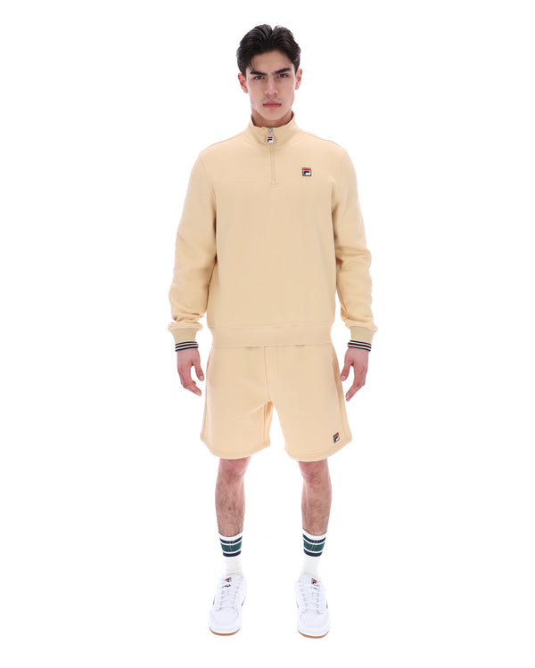 Man wearing a beige tracksuit with a brand logo on a white background