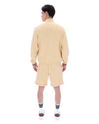 Man wearing a beige quarter zip jumper, paired with matching shorts, against a white background