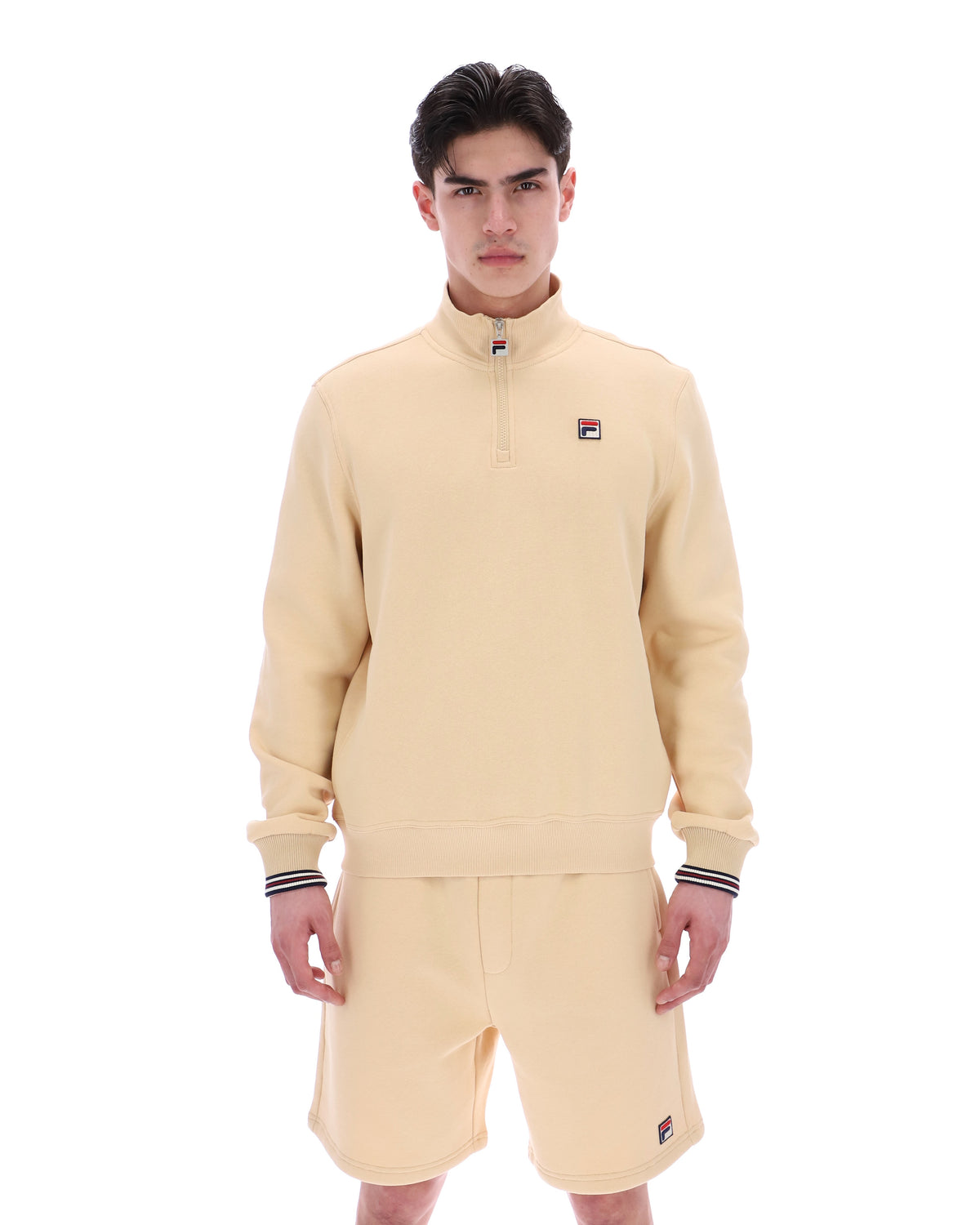 Man wearing a beige quarter zip jumper with a small FILA logo on the chest, paired with matching shorts, against a white background.