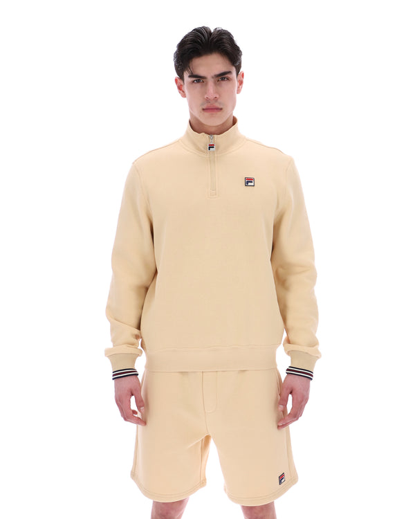 Man wearing a beige quarter zip jumper with a small FILA logo on the chest, paired with matching shorts, against a white background.