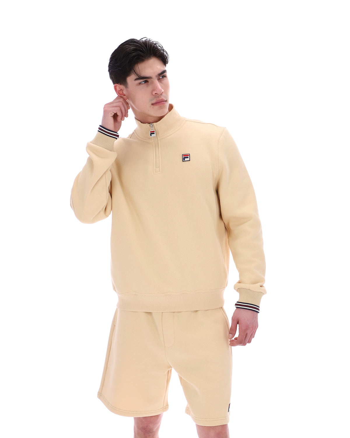 Man wearing a beige quarter zip jumper with a small FILA logo on the chest, paired with matching shorts, against a white background