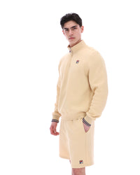 Man wearing a beige quarter zip jumper with a small FILA logo on the chest, paired with matching shorts, against a white background.