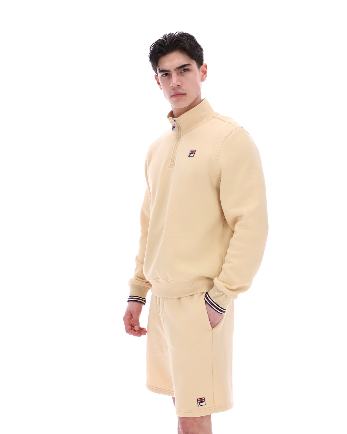 Man wearing a beige quarter zip jumper with a small FILA logo on the chest, paired with matching shorts, against a white background.