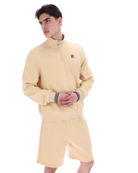 Man wearing a beige quarter zip jumper with a small FILA logo on the chest, paired with matching shorts, against a white background