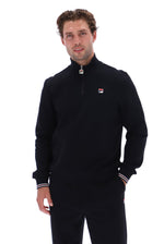 A man wearing a black Fila quarter-zip pullover sweater and matching black track pants, standing against a solid white background.