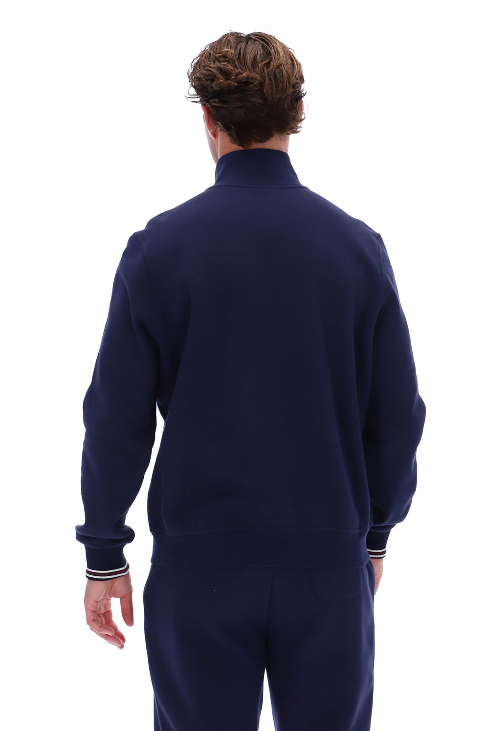 A man viewed from behind wearing a navy blue mock-neck sweatshirt and matching navy pants against a plain white background.