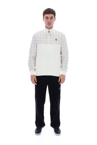 A man modeling a white and beige plaid zip-up jacket with a high collar, paired with black trousers and black sneakers, against a solid white background.