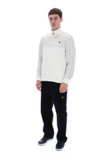 A man modeling a cream and beige plaid quarter-zip pullover sweater with black trousers and black sneakers, standing against a solid white background.