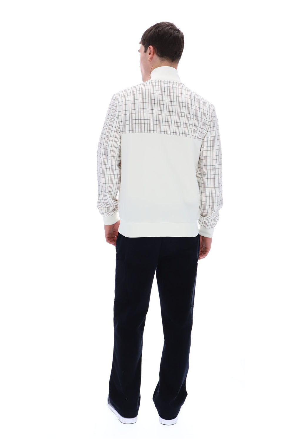 A man viewed from behind wearing a color-blocked quarter-zip pullover sweater with a cream and beige plaid pattern on the upper portion and sleeves, and a solid cream back panel. He is also wearing dark trousers and white sneakers, set against a plain white background.