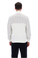 A man viewed from the back wearing a long-sleeve knit sweater with a white and beige plaid upper back and shoulders, a solid white lower back panel, and dark navy pants, against a plain white background.