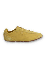 Profile view of a FILA Ritmo trainer in yellow suede, featuring a low-profile silhouette, matching laces, tonal stitching details, a subtle embossed 'F' logo on the side panel, and a slim brown rubber sole against a white background.