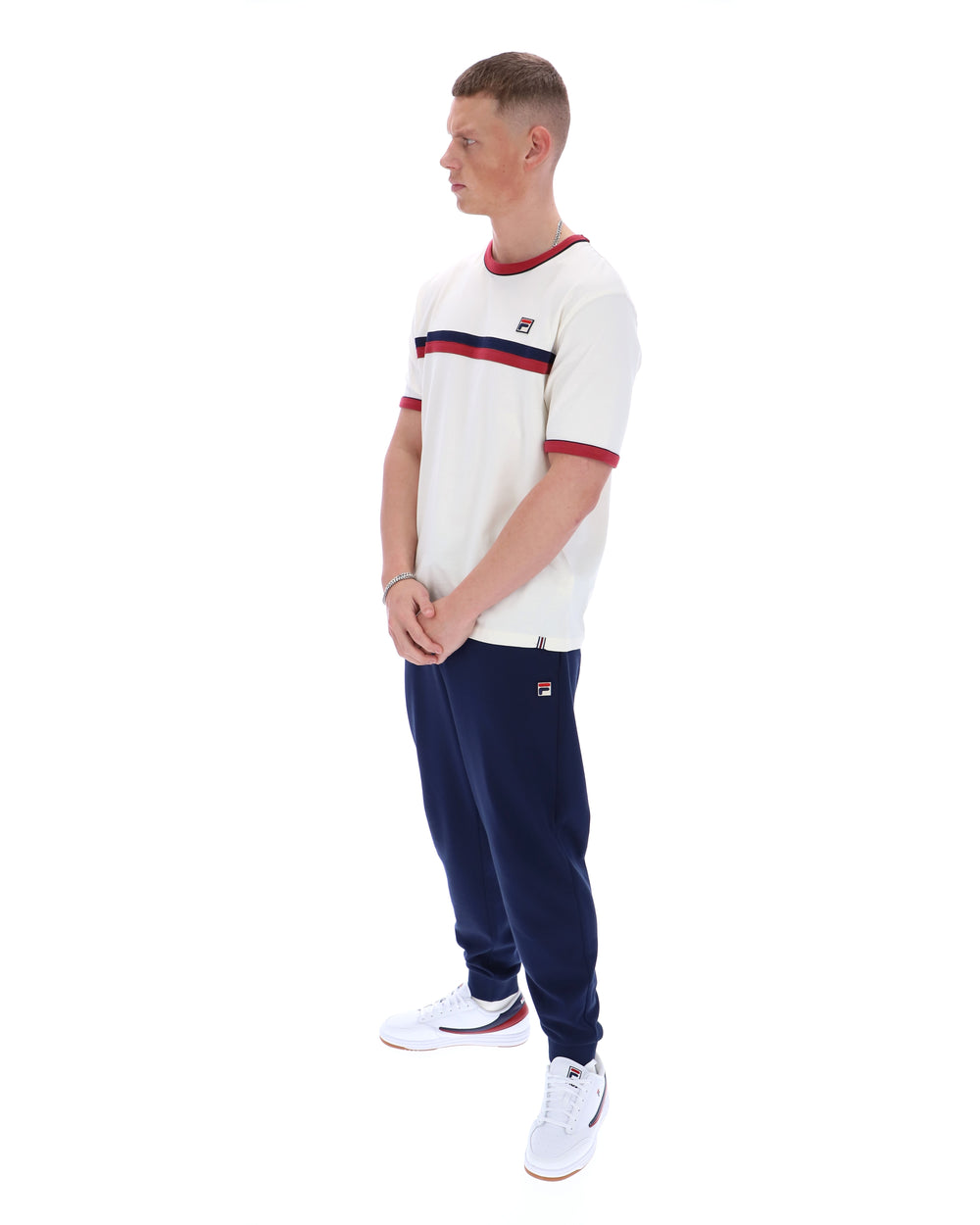 Man wearing a white t-shirt with red and blue stripes and navy tracksuit pants on a white background