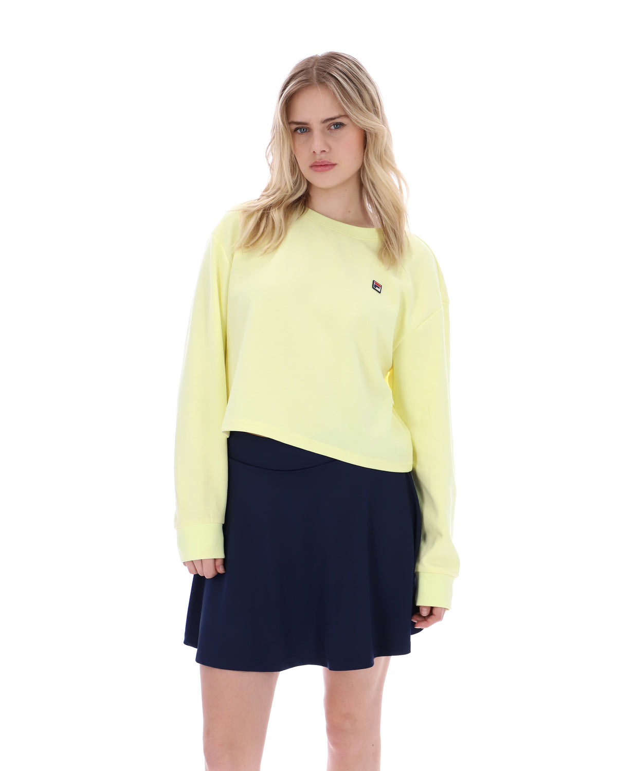 Woman wearing a light yellow sweater and navy skirt on a white background