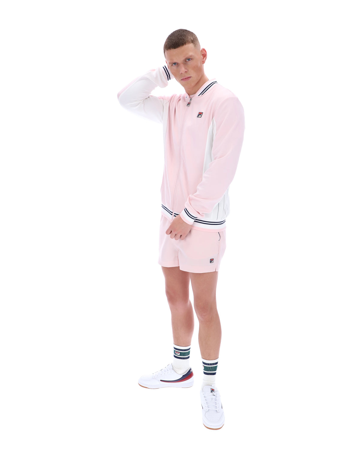 Person wearing a pink tracksuit with a FILA logo, paired with matching shorts on a white background