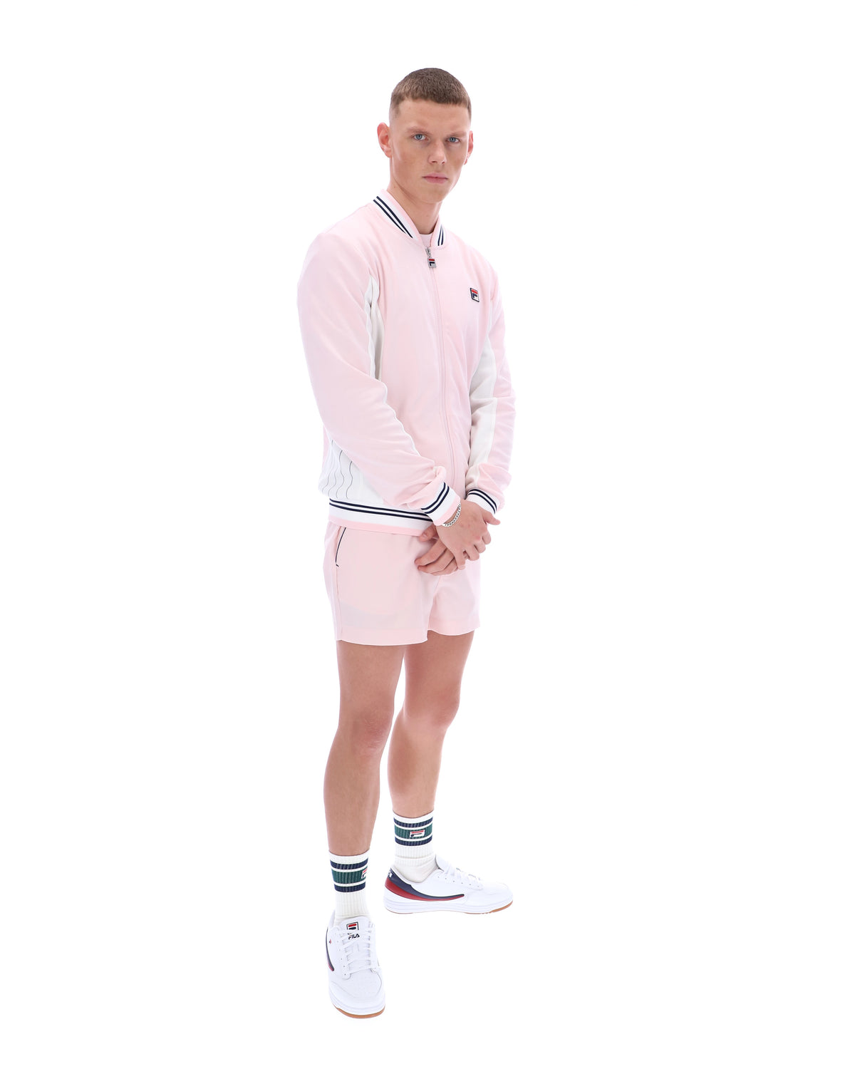 Person wearing a pink tracksuit with a FILA logo, paired with matching shorts on a white background